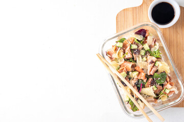 Healthy balanced sushi bowl lunch box with rice, nori, cucumbers, lettuce leaves, salmon fish and sesame, soy sauce and chopsticks