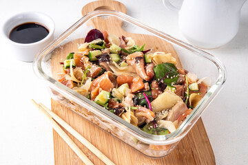 Healthy balanced sushi bowl lunch box with rice, nori, cucumbers, lettuce leaves, salmon fish and sesame, soy sauce and chopsticks