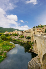 Obraz premium A stunning medieval town in Besalú, Catalonia, Spain, featuring the iconic stone bridge, historic buildings, lush green landscapes, and a serene river reflecting the picturesque scenery.
