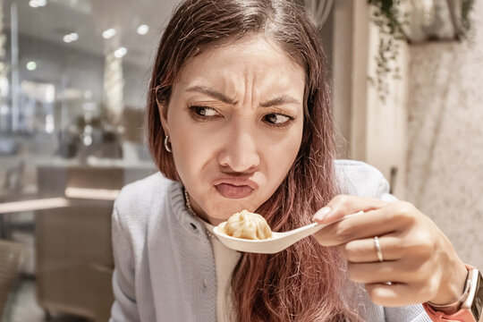 Young woman making a disgusted face while holding a spoon with a dumpling in a chinese restaurant