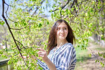 A beautiful girl is sitting on a bench by a lake. She is wearing a striped shirt and her hand is on her hip. The scene is peaceful and serene, the woman is enjoying the view of the water