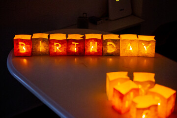 cardboard boxes illuminated with candles inside with letters cut out with the construction of the word happy birthday