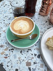 Coffee Break Bliss: Indulge in the creamy perfection of a latte art cappuccino, served in a cheerful yellow cup, atop a terrazzo table. A perfect moment of calm amidst a busy day.