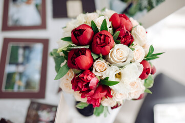 Obraz premium Close-up of a luxurious wedding bouquet featuring vibrant red peonies, white roses, and green foliage arranged in a classic design. 