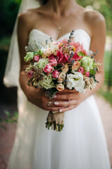 Colorful wedding bouquet with roses, greenery, and wildflowers held by a bride wearing a white wedding dress.