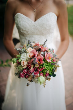 Colorful wedding bouquet with roses, greenery, and wildflowers held by a bride wearing a white wedding dress.

