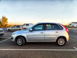 Silver hatchback parked in an empty lot during sunset near a quiet residential area © keleny