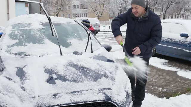 Father and son clean the car from snow with a brush.