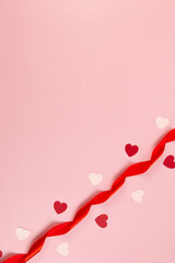 Top view of red ribbon, red hearts and pink hearts on pink background. Valentine's day, love. Shiny rolled fabric, silk and satin material. Copy space, flat lay.