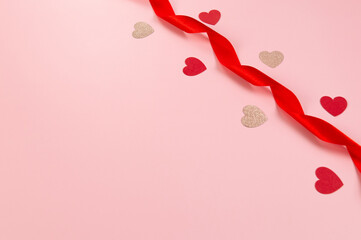 Top view of red ribbon, red hearts and pink glitter hearts on pink background. Valentine's day, love. Shiny rolled fabric, silk and satin material. Copy space, flat lay.