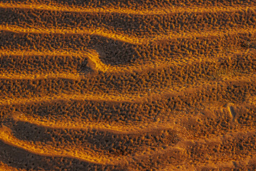 Close-up of textured sand ripples illuminated by warm sunlight, creating a striking pattern of light and shadow. The natural formations highlight the beauty of wind-shaped landscapes.
