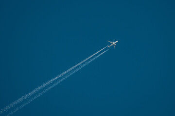 A high-altitude airplane soars through a deep blue sky, leaving behind two distinct contrails. The image captures the beauty of air travel and aviation dynamics. Copy space included.
