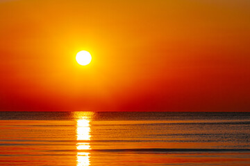 A mesmerizing sunset over the ocean, casting golden and orange hues across the sky and water. The sun’s reflection creates a serene and warm atmosphere.