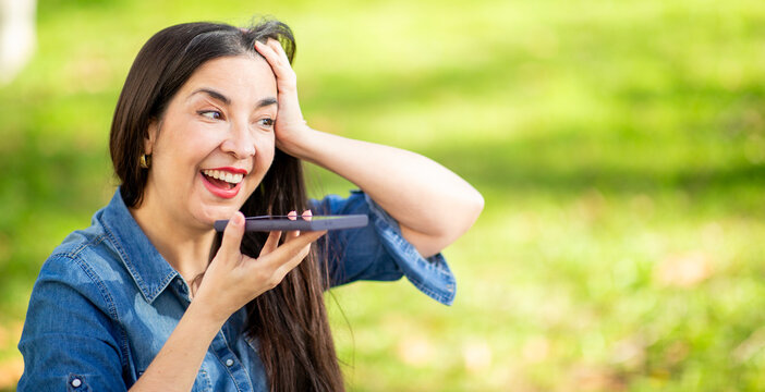 Friendly mature woman recording a voice message on her phone in a park