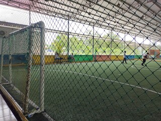 Fototapeta premium Kendari, Indonesia- February 8, 2025: Futsal Field Safety Net, goalposts, and players. The steel structure of the field building is visible.