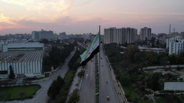 New Syrian Flag Waves on a Towering Pole in a Public Square. Syrian revolution against Bashar al-Assad.