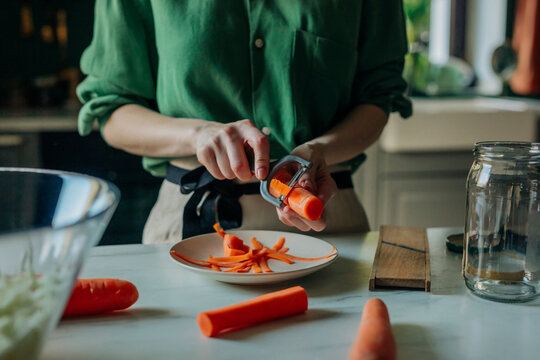 Woman preparing carrots for sauerkraut in a home kitchen