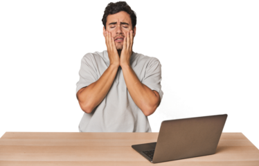 Hispanic young man working on laptop crying, unhappy with something, agony and confusion concept.