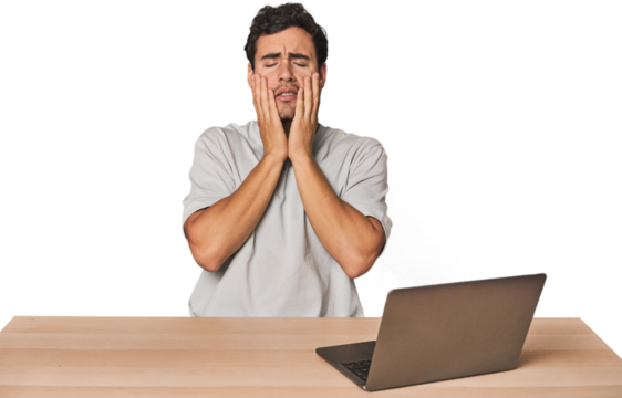 Hispanic young man working on laptop crying, unhappy with something, agony and confusion concept.