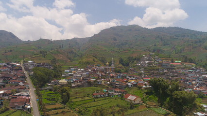 asian town with mosque in mountains among agricultural land, rice terraces. mountains with farmlands, rice fields, village, fields with crops, trees. Aerial view farm lands on mountainside. tropical