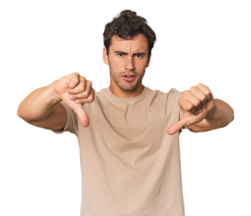Young Hispanic man in studio showing thumb down and expressing dislike.