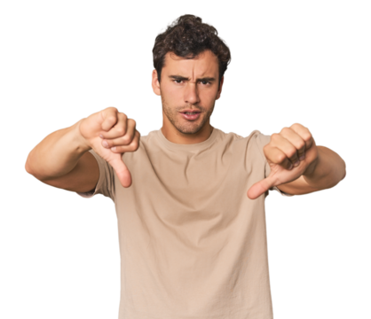 Young Hispanic man in studio showing thumb down and expressing dislike.