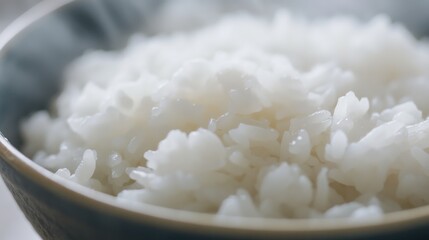 Close-up of a bowl of cooked rice. Featuring fluffy white rice with steam rising. Emphasizing the texture and appetizing appearance. Ideal for recipes and food presentations.