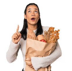 Young Filipina shopping for groceries pointing upside with opened mouth.