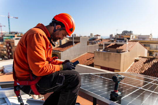 Smiling construction worker using smart phone near solar panel on rooftop
