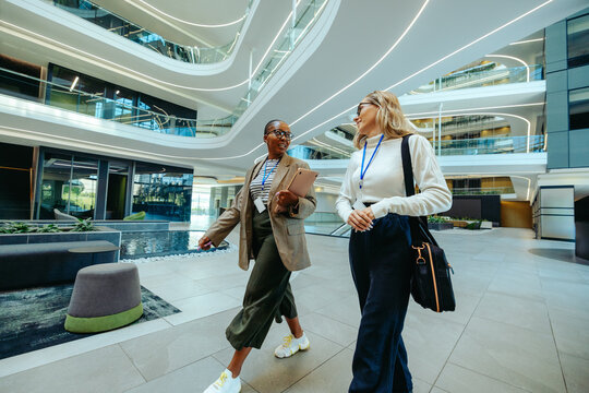 Two female colleagues walking and chatting in modern office space - Powered by Adobe