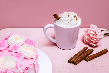 A delicate pink dessert with a slice of cake and a cup of hot chocolate with whipped cream, garnished with cinnamon and a flower, on a pastel background.