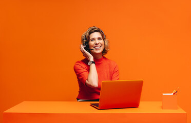 Happy call center agent in a vibrant monochromatic orange workspace, emphasizing creativity and customer care