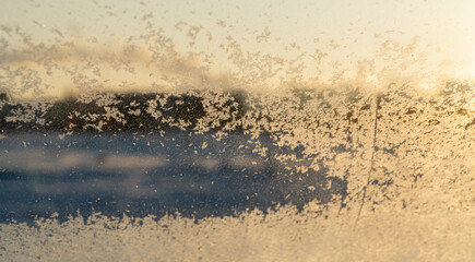 Frost patterns on the window, hoarfrost background. Frosty Christmas pattern on the winter window glass. The windshield of the car is covered with snowflakes.  