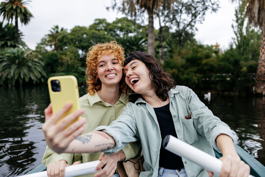 Happy couple rowing boat and taking selfie through smart phone in lake - Powered by Adobe