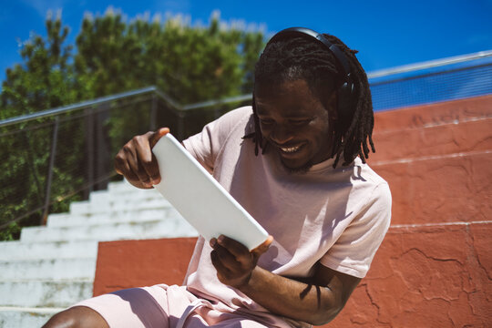 Smiling young man wearing wireless headphones and playing video games on tablet PC