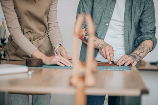 Businesswoman with businessman cutting leather patch at workbench