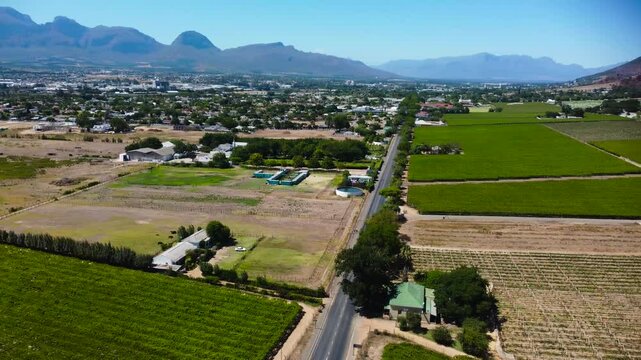 Camera panning left to right across the vineyards and main road leading into Paarl Town South Africa with the iconic Paarl rock and the Mountain range behind the town 4K aerial video
