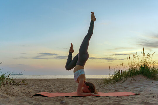 Practicing yoga in a headstand position on the beach during sunset with a tranquil atmosphere