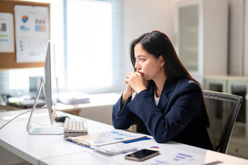 Obraz premium A woman is sitting at a desk with a computer monitor and a stack of papers