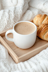 A close-up of a cozy bed setting where a small wooden tray carries a cup of hot coffee and a couple