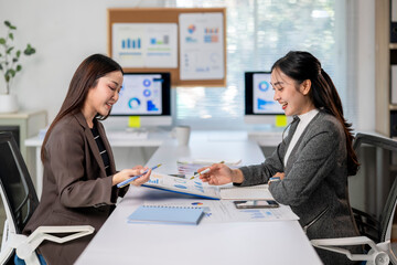 Two women are sitting at a desk with a white board behind them
