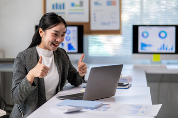 A woman is sitting at a desk with a laptop and a stack of papers