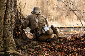 Historical reconstruction. German Wehrmacht Infantry soldier during the Second World War fight in the forest. View from the back