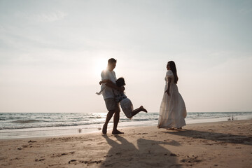 Happy asian family enjoy together on the beach in holiday vacation. Silhouette of the family holding hands enjoying the sunset on the sea beach. Happy family travel, trip  family holidays weekend.