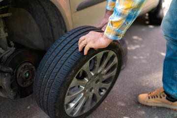 Obraz premium Man replaces tire on a car while parked on a roadside during daylight
