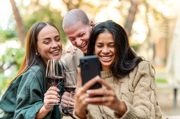 Young friends having fun drinking red wine at winery bar - Happy people sharing content on mobile phone together at open air restaurant garden - Food, beverage and Tech, modern life style concept