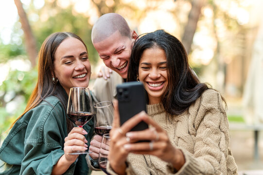 Young friends having fun drinking red wine at winery bar - Happy people sharing content on mobile phone together at open air restaurant garden - Food, beverage and Tech, modern life style concept