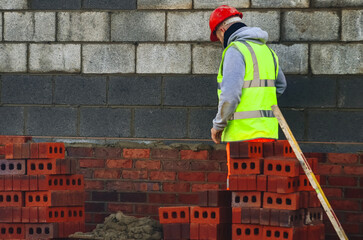 Bricklayer working diligently on a construction site, wearing a safety helmet and reflective vest...