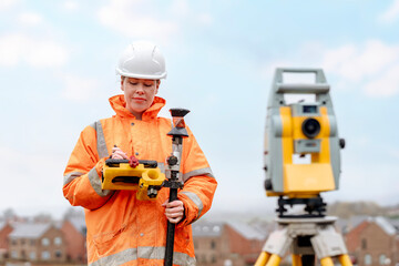 Female Surveying professional at work using a total station in a construction area on a clear day...