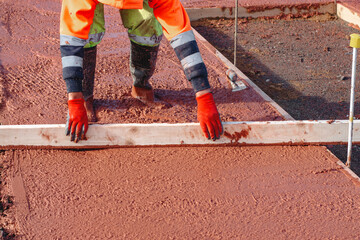 Builder leveling  a concrete slab at a construction site, ensuring a smooth finish and proper...